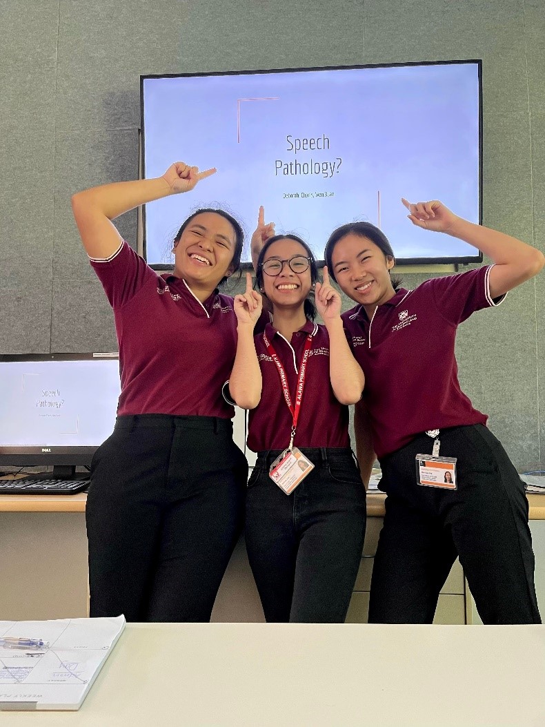 Three speech pathology students pointing at a screen that reads speech pathology