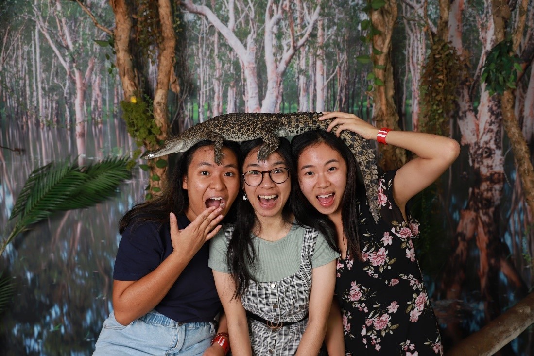 Three speech pathology students holding a crocodile on their heads