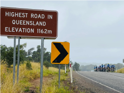 Cyclists riding past a sign labelled highest road in Queensland elevation 1162m