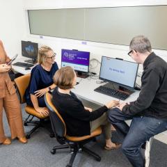 Four people gathered around a computer that is assisting the user with aphasia-friendly technology
