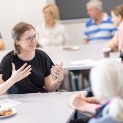 Young person at a desk speaking with an older couple in a room full of other people